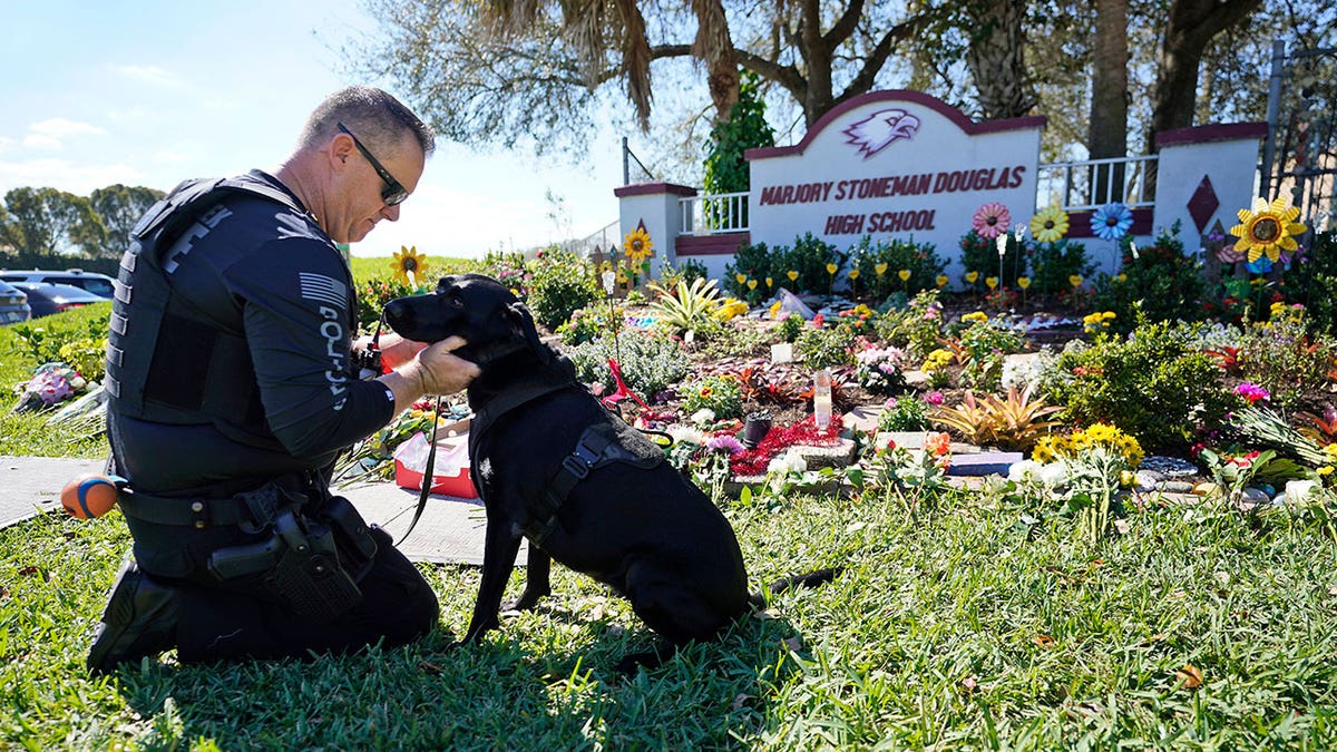 Police officer with dog kneeling in front of Parkland shooting memorial
