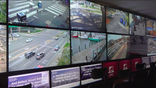 Multiple TV screens playing security camera footage, including busy streets and neighborhoods