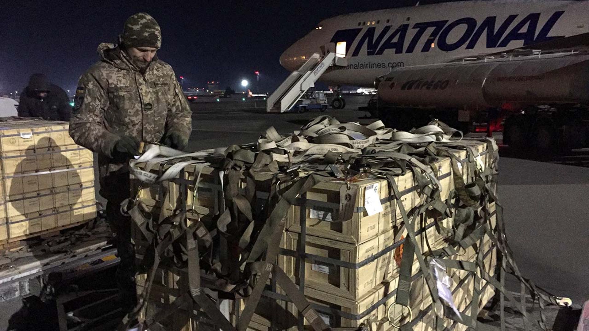A man in military gear unloads a plane.