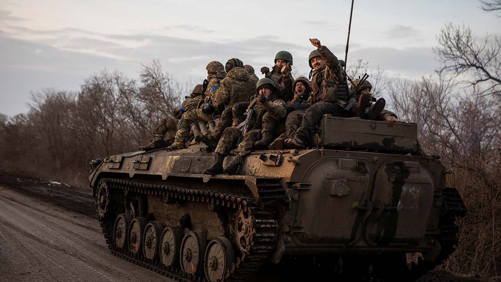A group of military men ride on a tank.