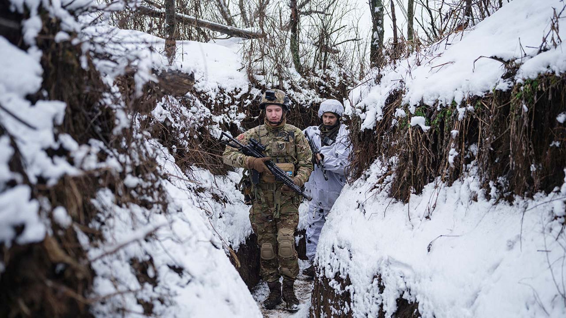 Men in military gear walk through snow.