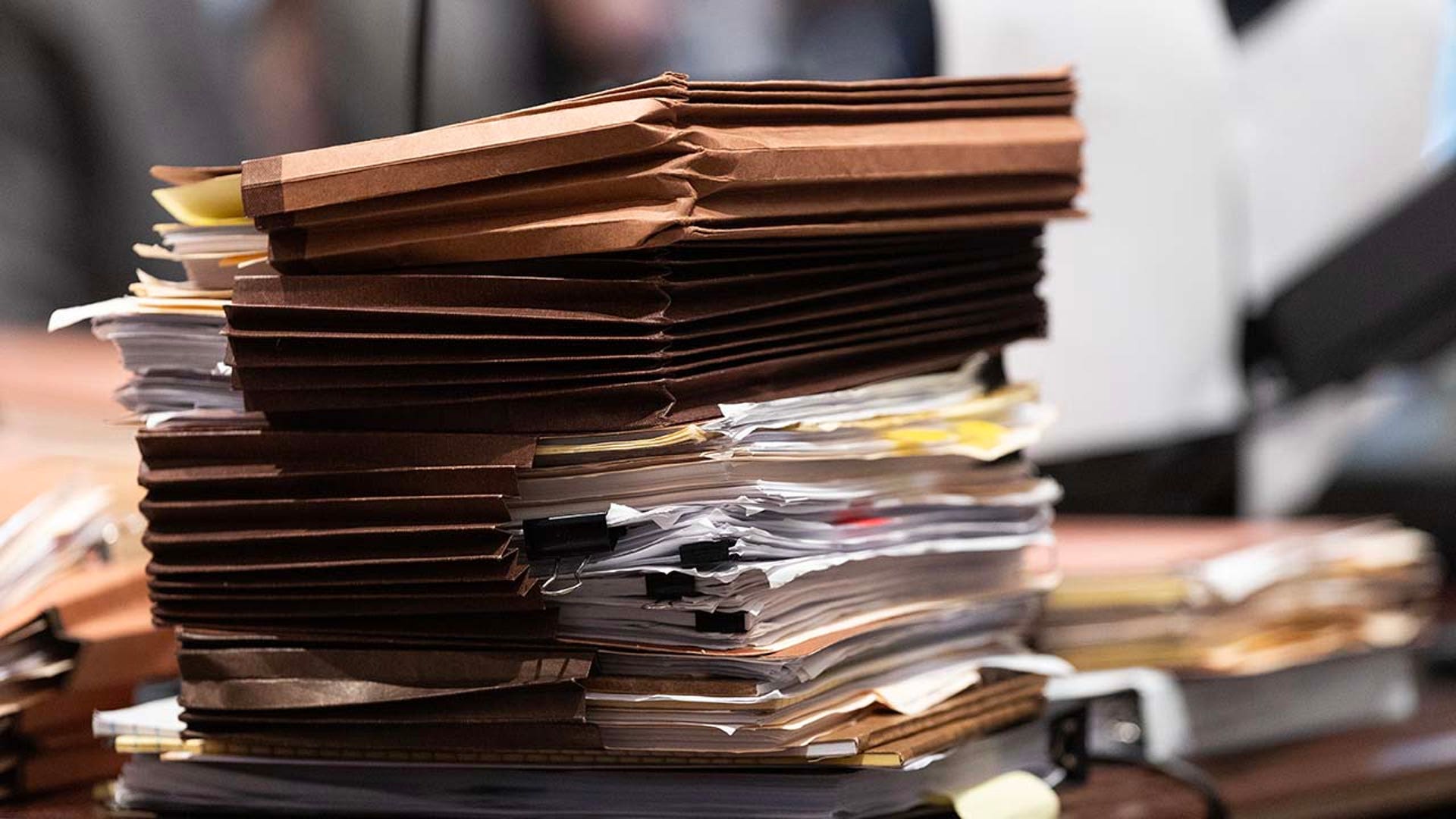 A stack of paperwork sits on a desk inside a courtroom.