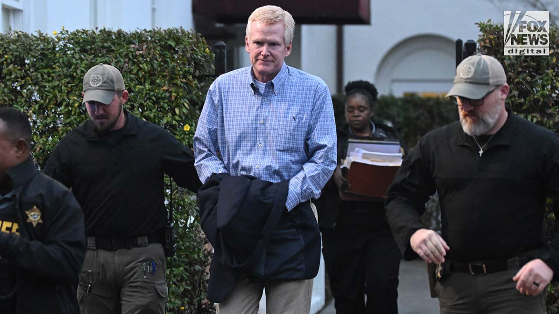 A man exits a courthouse surrounded by police.
