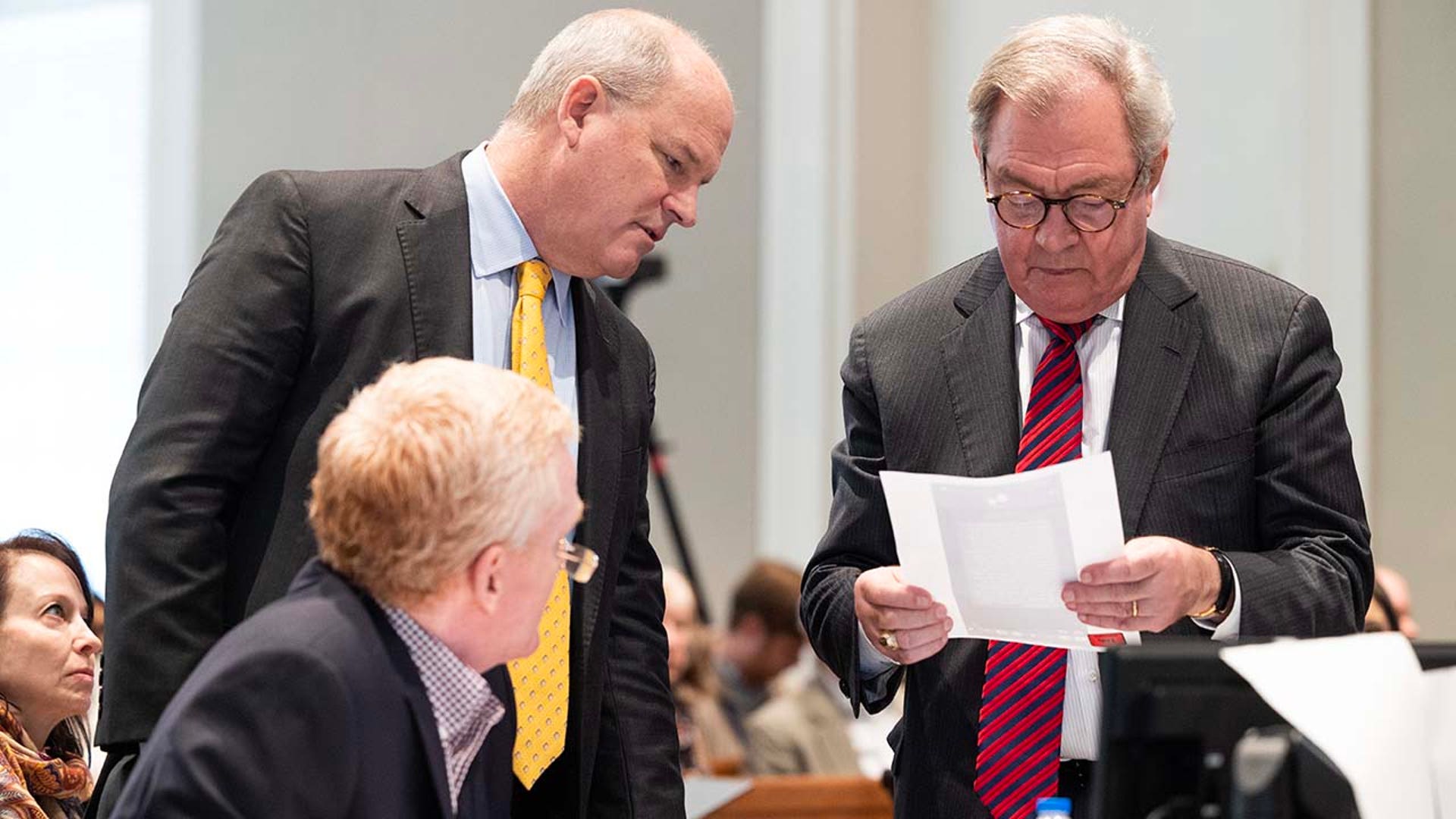 Two men read a piece of paper in a courtroom.