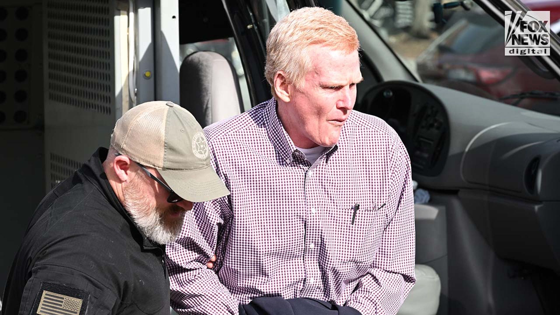 A man in a dress shirt is escorted out of a police van.