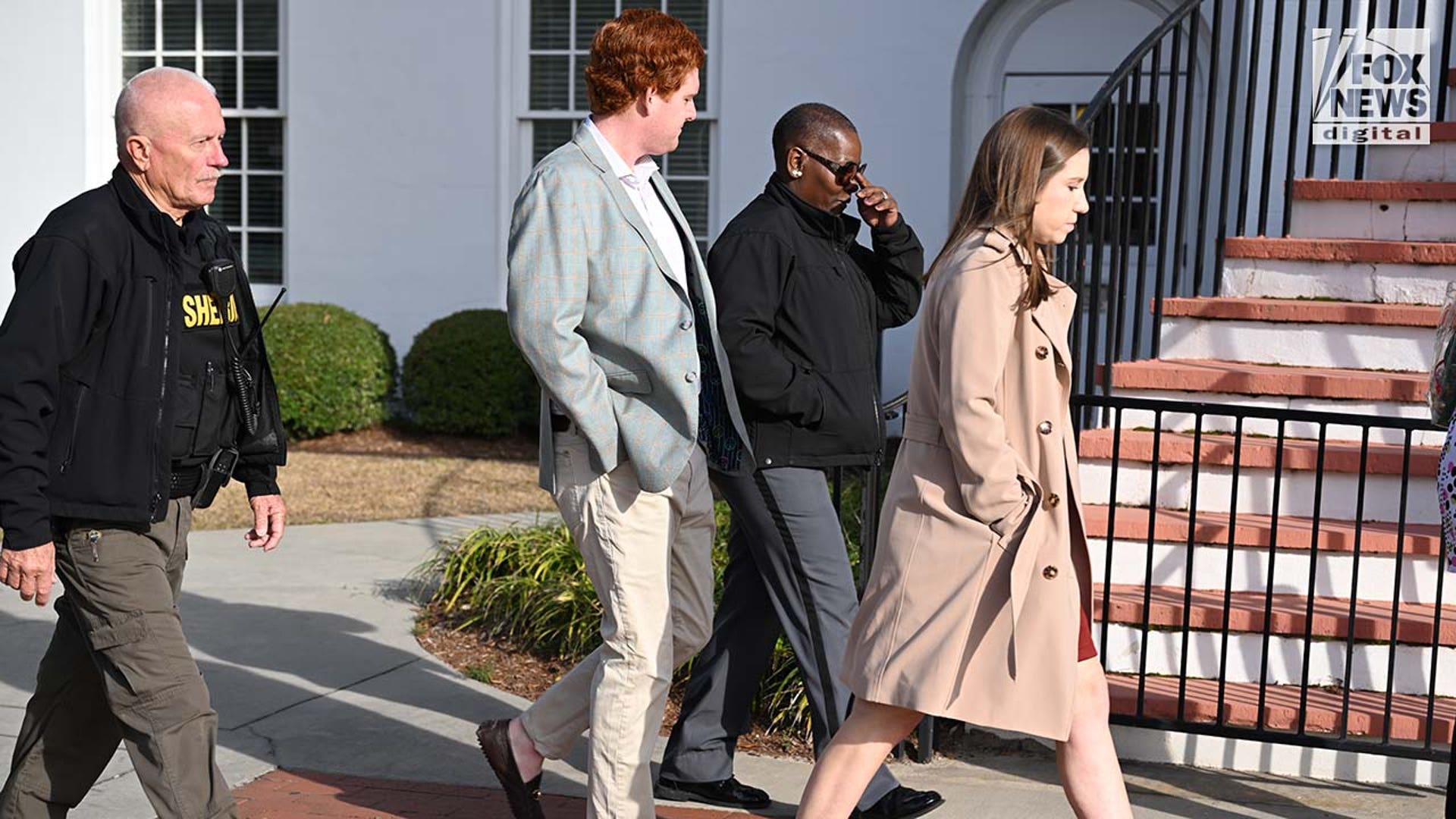 Four people walk outside, into a courthouse.