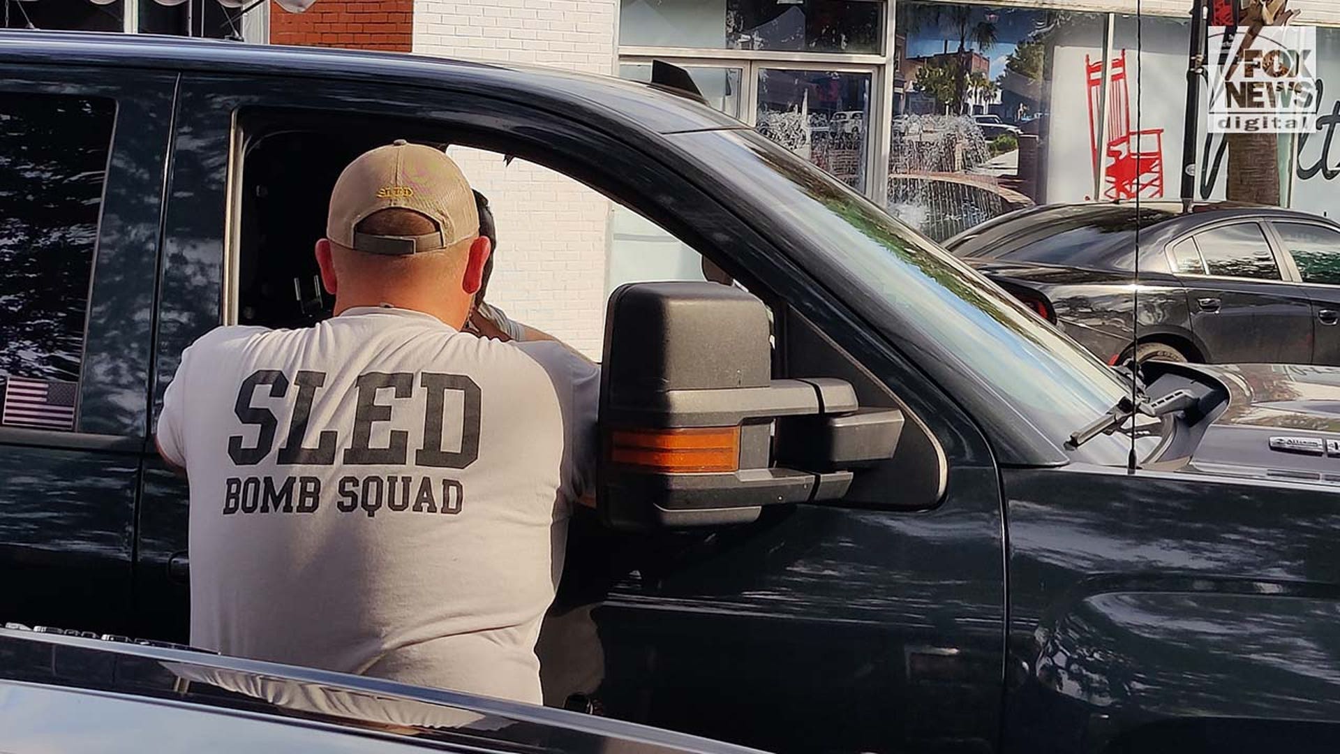 A bomb squad officer leans up against a car.