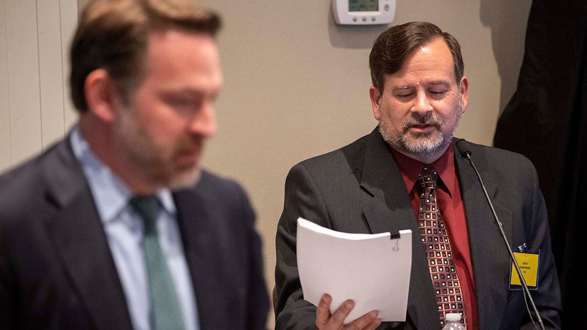 A man reads from paperwork on the witness stand in a trial.