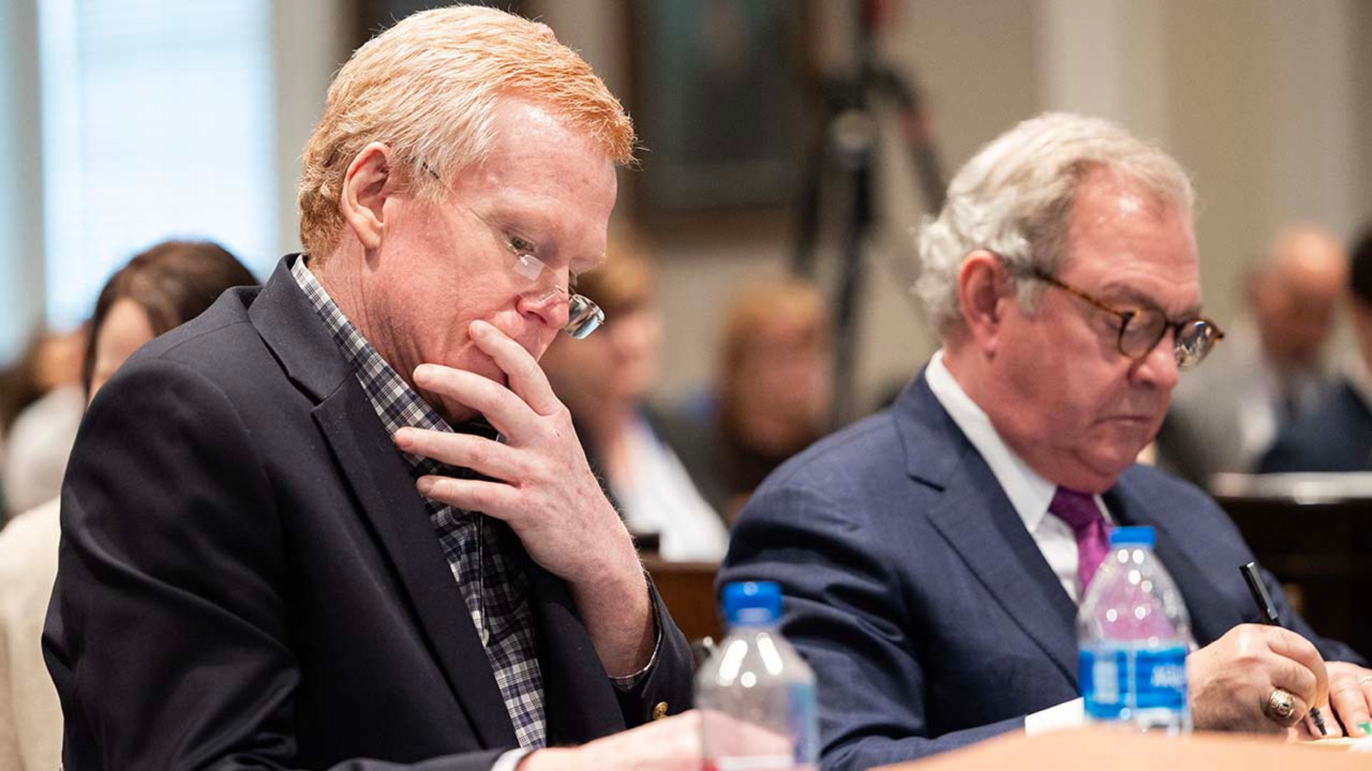 Two men examine paperwork inside a courtroom.