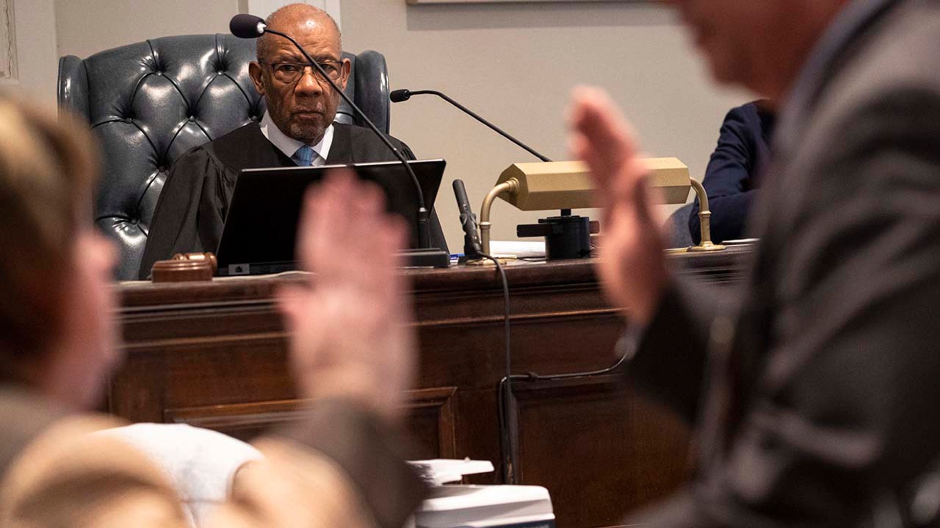 A judge watches as a man administers an oath in a courtroom.