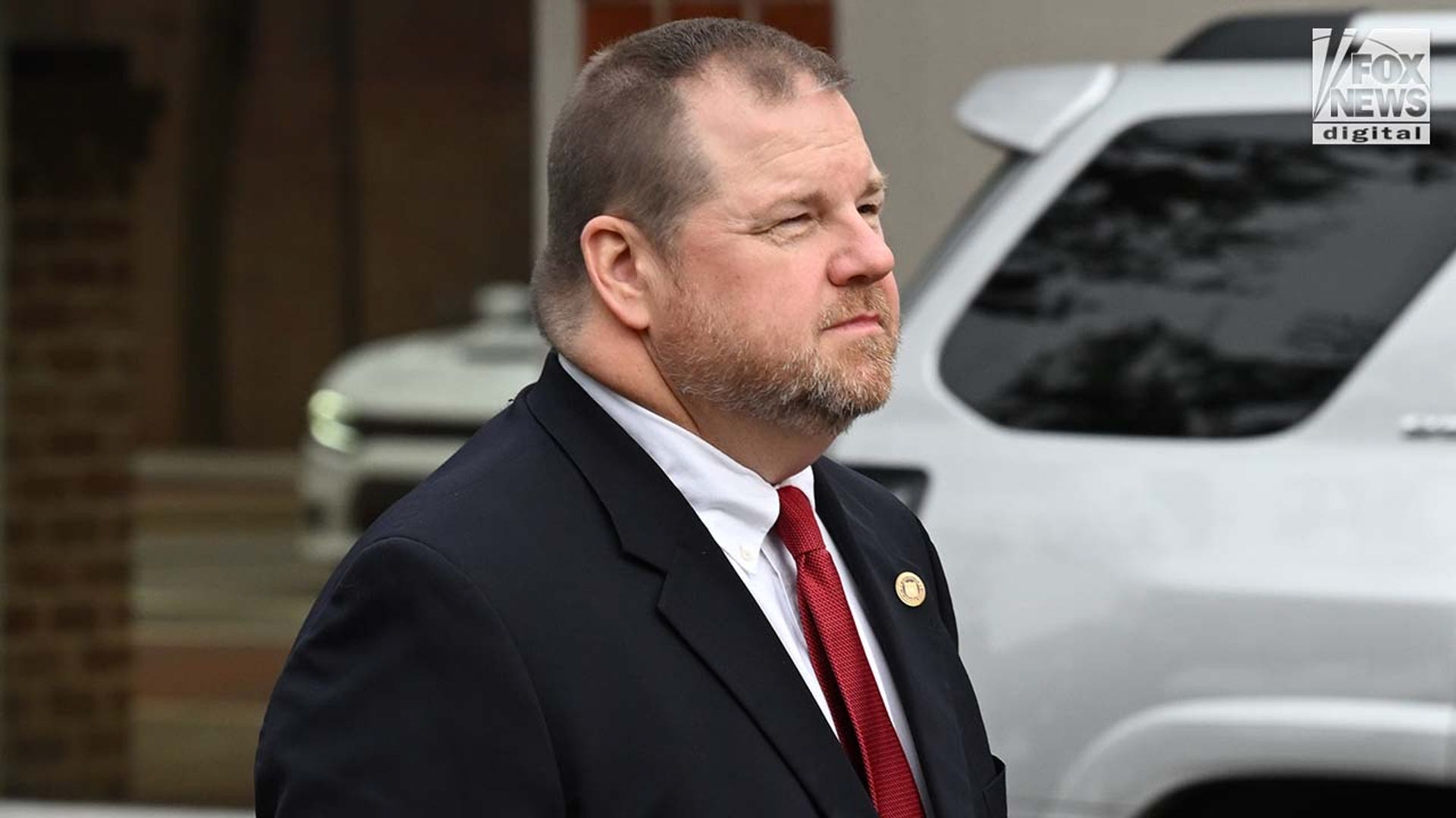 A man wearing a suit and red tie enters a courthouse.