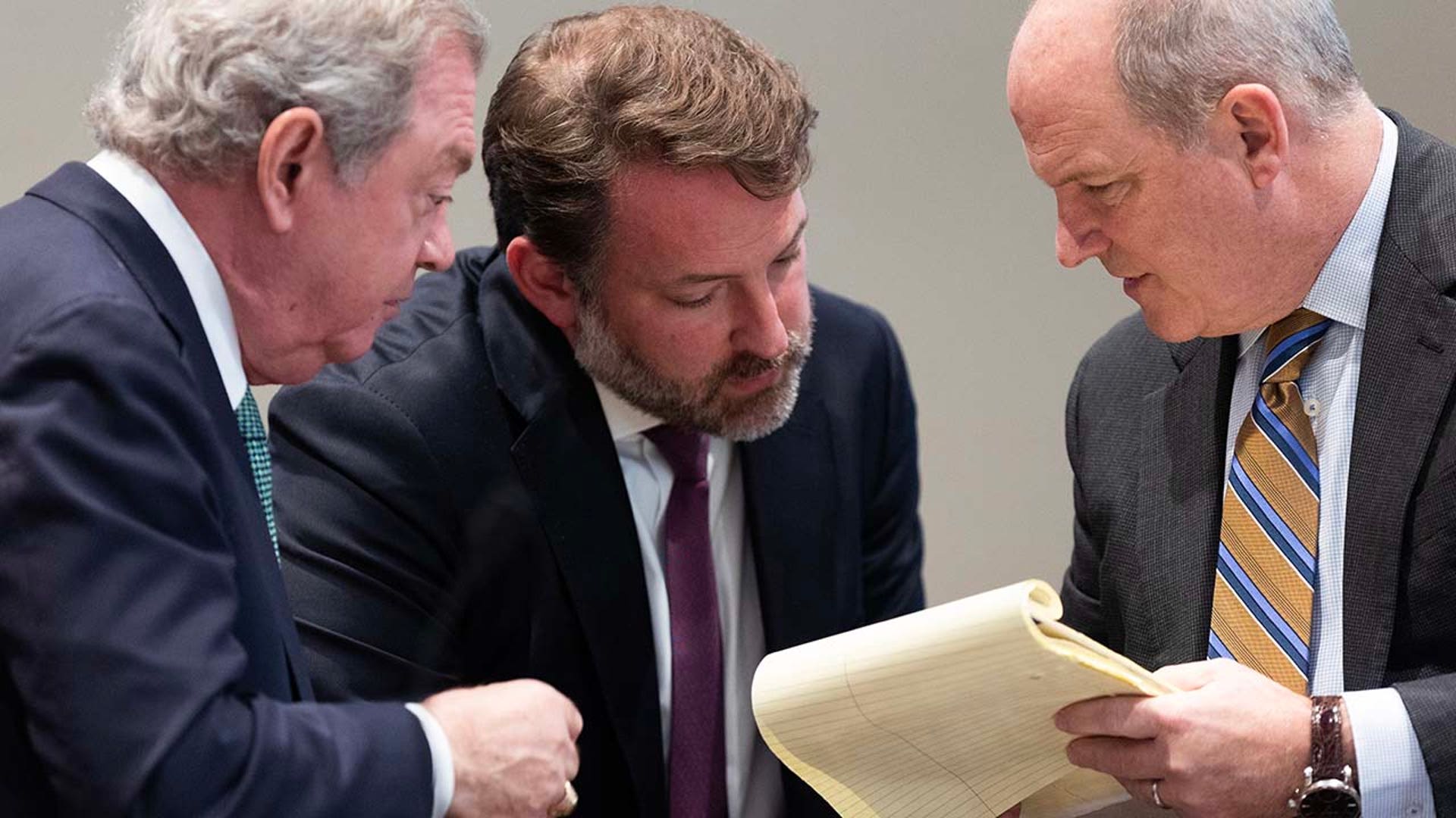 Three men speak to each other inside a courtroom.