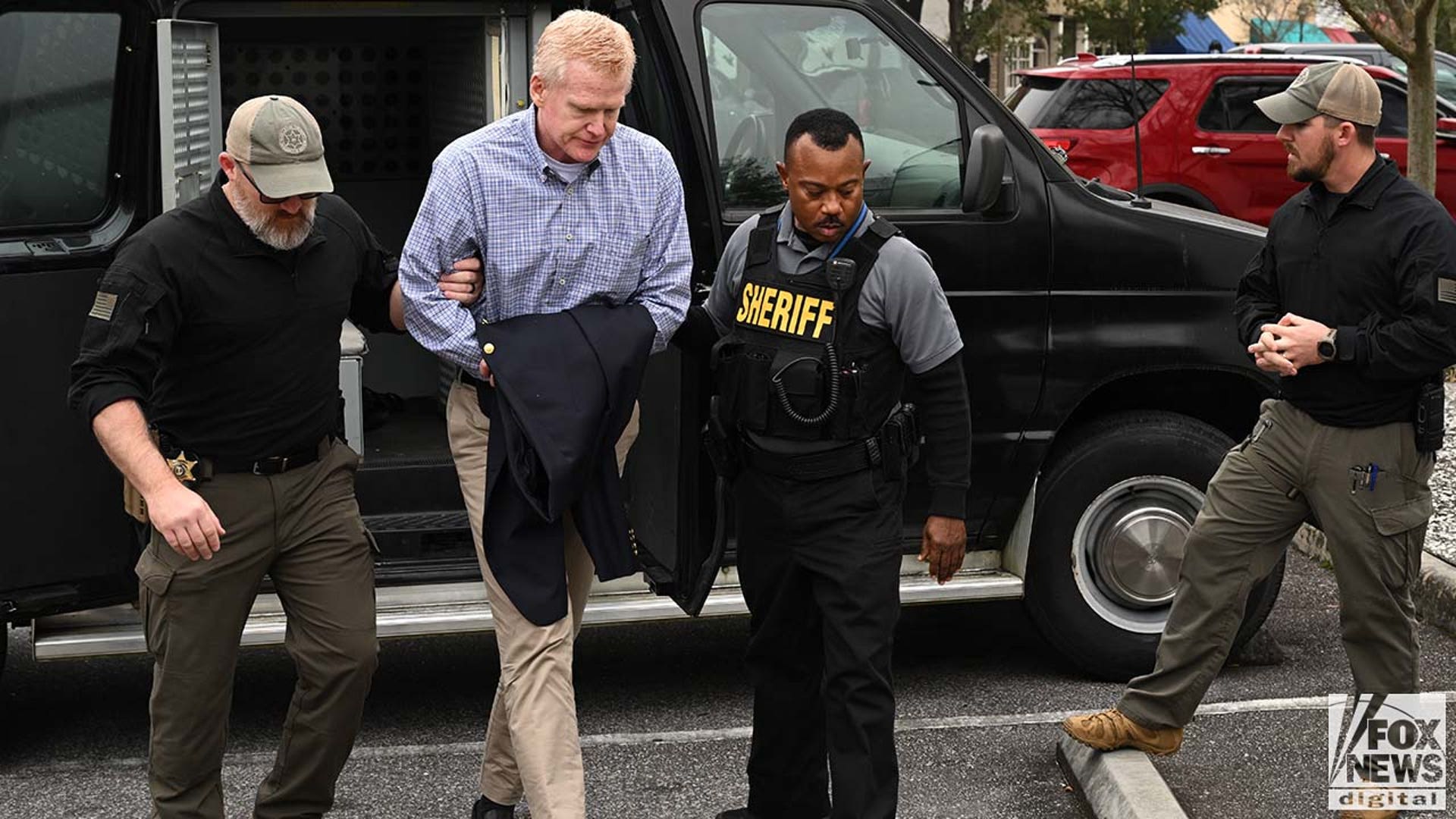 A man wearing a striped dress shirt is escorted into a courthouse by police.