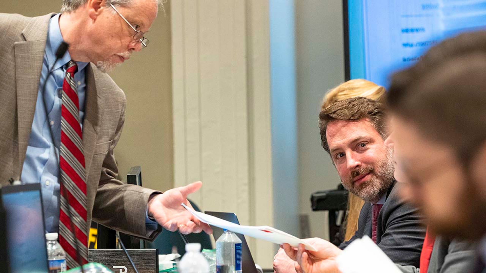 Two men hand off papers while inside a courtroom.