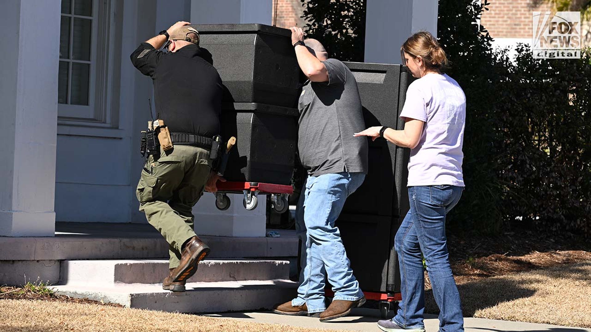 Three people carry boxes of food into a courthouse.