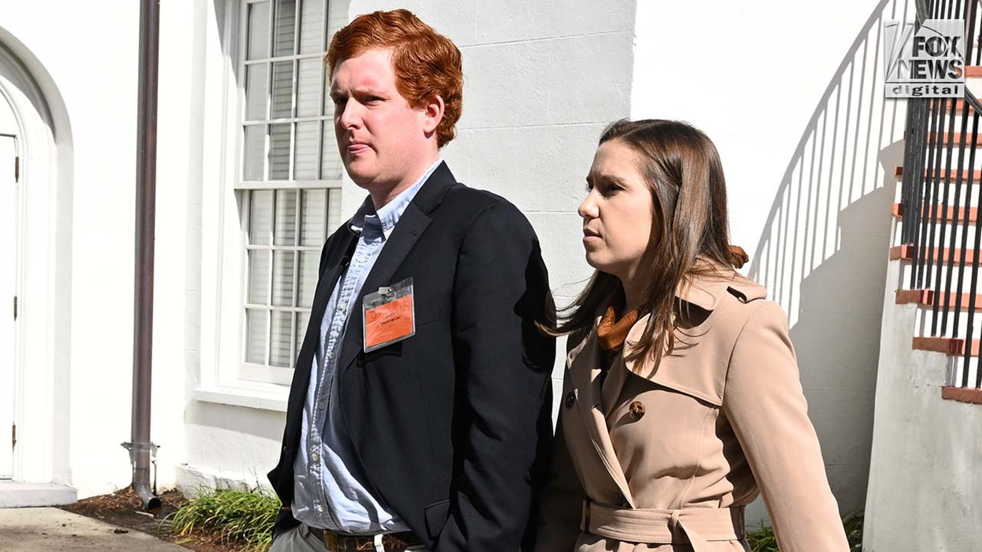 A man wearing a suit and a woman wearing a coat exit a courthouse.