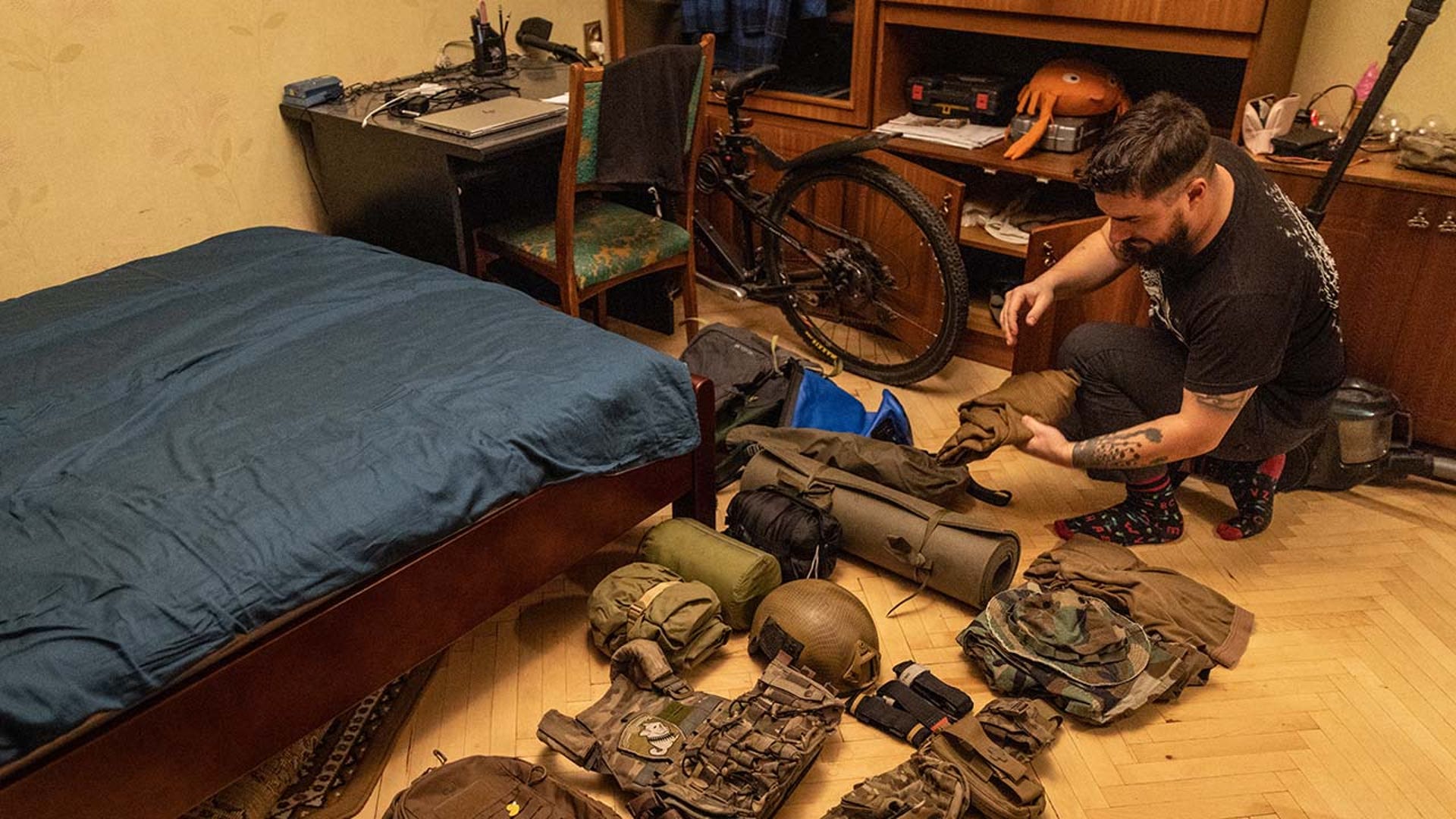 A man lays military gear on his bedroom floor.