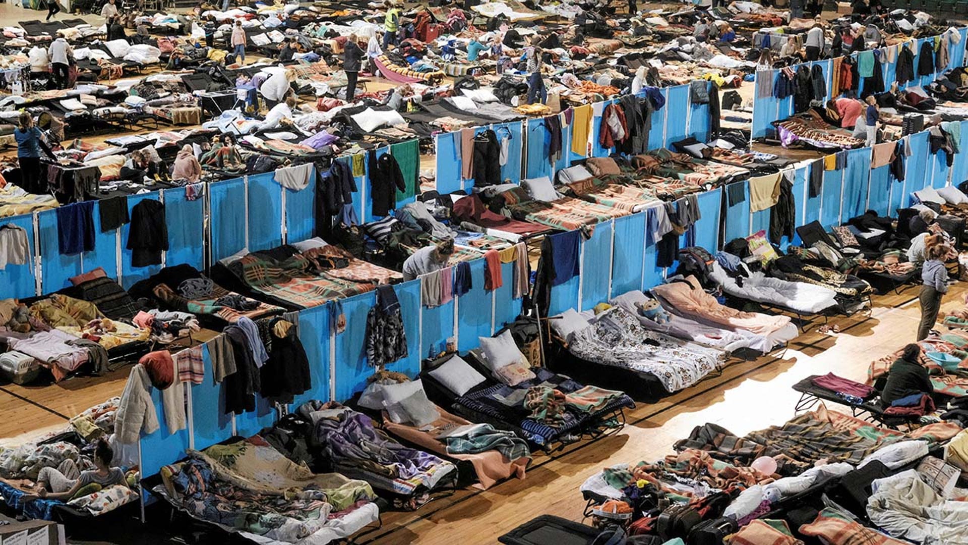 Hundreds of people sleep on cots inside of an arena.