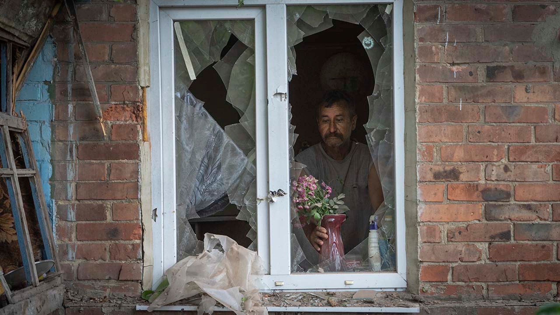 A man places flowers in a broken windowsill.