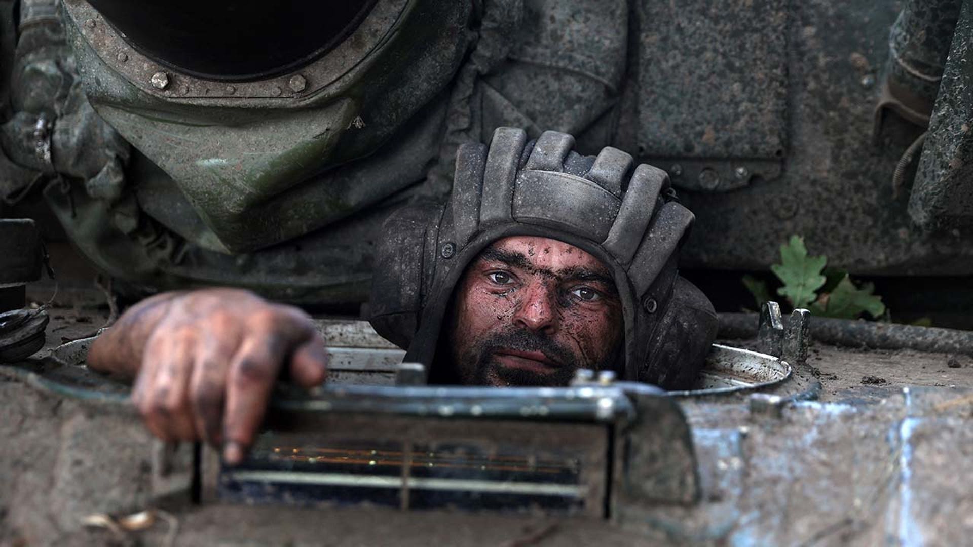 A man wearing a helmet peers out of a military vehicle.