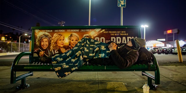 Unhoused Mario Lopez sleeps on a bus stop bench in Echo Park.