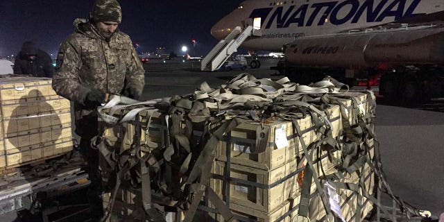 A man in military gear unloads a plane.
