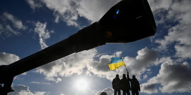 Ukrainian personnel hold a Ukrainian flag as they ride a Challenger 2 tank during training at Bovington airfield in southwest Britain, February 22, 2023.