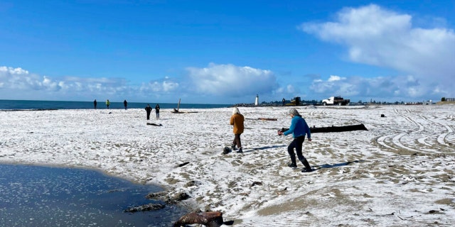 People walk along a snow-covered Twin Lakes State Beach in Santa Cruz, California, on Thursday, Feb. 23, 2023.