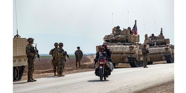 Members of a family ride a motorcycle as a U.S. military convoy patrols the area near the town of Tal Hamis, southeast of the city of Qameshli in Syria's northeastern Hasakeh governorate, Jan. 26, 2023. 