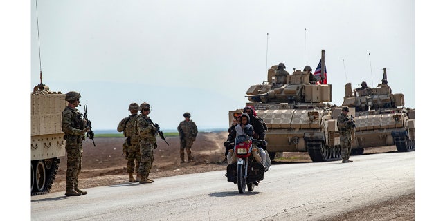 Members of a family ride a motorcycle as a U.S. military convoy patrols the area near the town of Tal Hamis, southeast of the city of Qameshli in Syria's northeastern Hasakeh governorate, Jan. 26, 2023. 