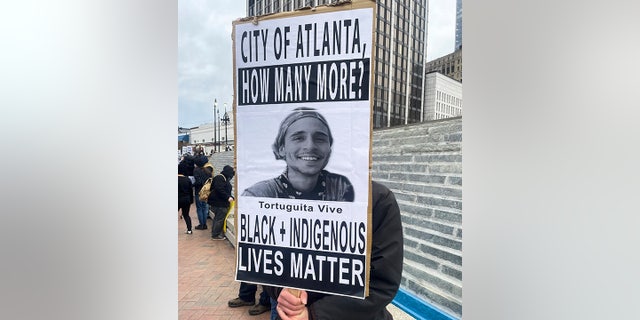 A demonstrator holds a sign protesting the death of an environmental activist in Atlanta. His family is now suing for more information about the shooting.