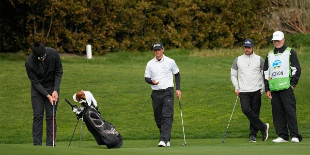 Beau Hossler, left, putts on the 13th green of the Pebble Beach Golf Links as Max McGreevy, center, and Lukas Nelson, second from right, look on during the second round of the ATT Pebble Beach Pro-Am golf tournament in Pebble Beach, Calif., Friday, Feb. 3, 2023. A caddie for one of the amateurs in the group collapsed on the 11th fairway and was rushed to the hospital.