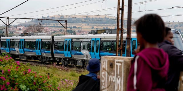 Pedestrians watch a train traveling from Johannesburg to Naledi in Soweto, South Africa, Wednesday, Feb. 8, 2023.