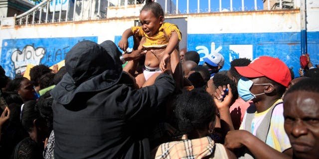 A parent tries to hand off his daughter to get her through the gate of Haiti´s immigration office as they wait their turn to apply for a passport, in Port-au-Prince, Haiti, Thursday, Feb. 9, 2023. 