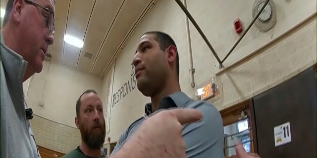 This photo provided by Ohio State Highway Patrol shows police bodycam footage of NewsNation correspondent Evan Lambert interaction with authorities Wednesday, Feb. 8, 2023 in the gymnasium of an elementary school in East Palestine, Ohio.