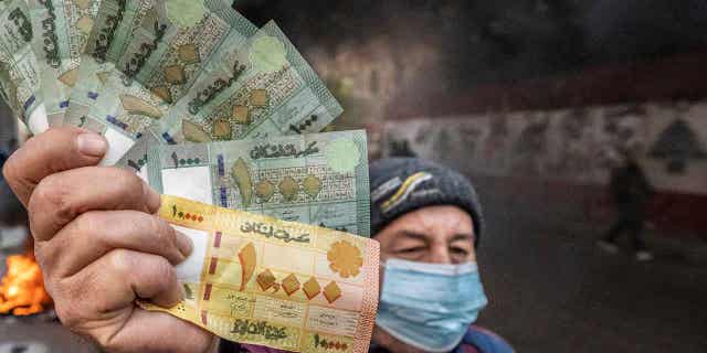 Lebanese pounds are shown in front of burning tires, in front of the country's Central Bank building, where the anti-government demonstrators rally against the Lebanese Central Bank Governor Riad Salameh.
