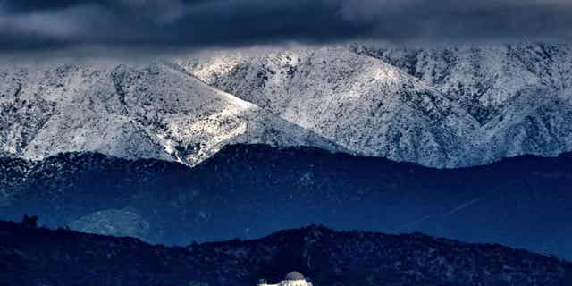 Storm clouds and snow are seen over the San Gabriel mountain range in Los Angeles on Feb. 26, 2023. A winter storm that swept the West Coast with flooding and frigid temperatures has shifted to southern California.