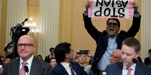 A protester interrupts H.R. McMaster, former national security adviser to former President Trump, as testifies during a hearing of a special House committee dedicated to countering China, on Capitol Hill, Tuesday, Feb. 28, 2023, in Washington. At right is Matthew Pottinger, former deputy national security adviser to former President Trump.