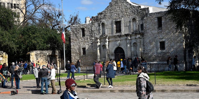 A tourist uses her phone and relaxes with her dogs in front of Mission San Antonio de Valero, better known as the Alamo, on Dec. 9, 2018. The former Franciscan mission was the site of the Battle of the Alamo in 1836 during Texas' war for independence from Mexico; Texan defenders were defeated by Mexican troops under General Antonio Lopez de Santa Anna. 