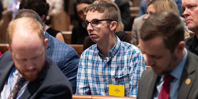 A man sits in the gallery of a courtroom.