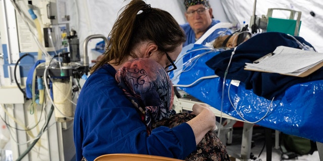 A Samaritan's purse nurse hugs a patient as they sit near a baby struggling with respiratory issues as a result of the earthquakes in Turkey.