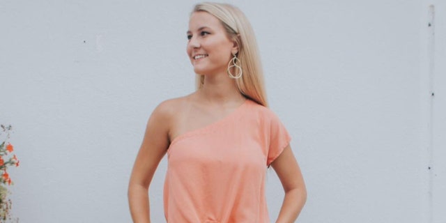 Mallory Beach smiles in a pink blouse with blonde hair and earrings