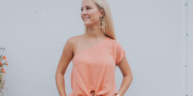 Mallory Beach smiles in a pink blouse with blonde hair and earrings