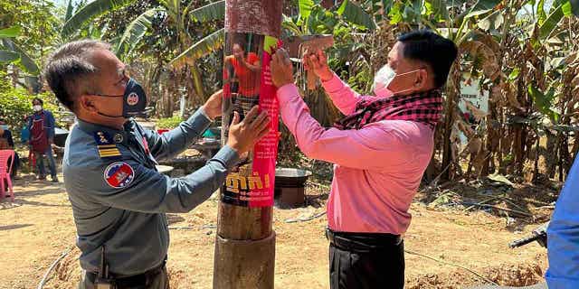 In this photo released by the Cambodia Ministry of Health, a Cambodia animal health officer, right, and a military police officer place posters about awareness of H5N1 virus threats in hopes of educating villagers to take care of their health in Prey Veng eastern province Cambodia, Feb. 23, 2023.