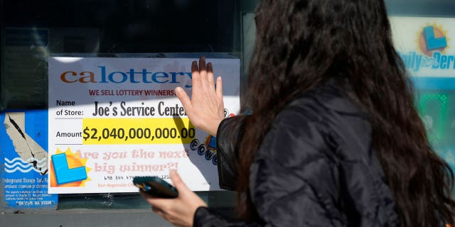 People touch a window sign for good luck announcing the $2.04 billion-winning Powerball ticket award at Joe's Service Center, a Mobil gas station at Woodbury Road and Fair Oaks Avenue in Altadena, CA., on Jan. 6, 2023.