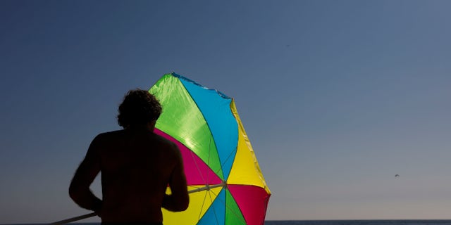 Seorang pria melipat payungnya di Laguna Beach, California, pada 7 Agustus 2018. Dewan kota Laguna Beach memilih untuk melarang balon guna mengurangi risiko kebakaran hutan dan polusi yang akan dimulai pada 2024.