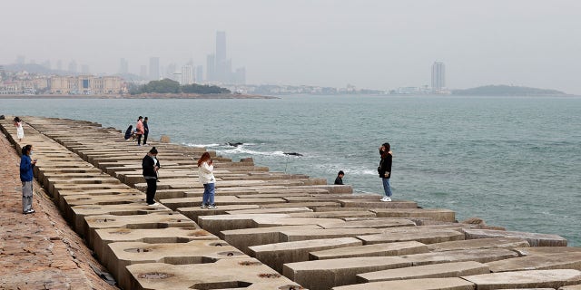 A visitor poses for pictures on the coast of Qingdao, Shandong province, China, following an oil spill in the Yellow Sea caused by a collision between tanker A Symphony and bulk vessel Sea Justice off Qingdao port, April 29, 2021.