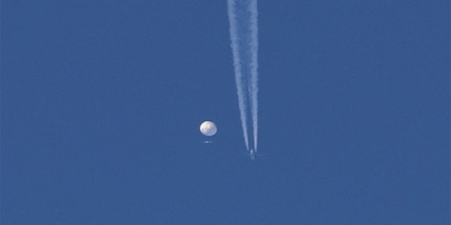 A large balloon moves over the Kingston, North Carolina area with an airplane and its contrail visible below it. 