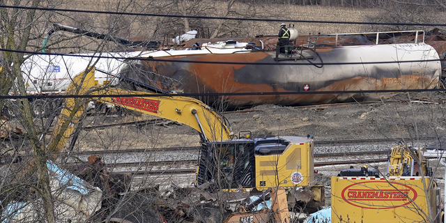 Workers are seen on Tuesday, Feb. 21, cleaning up derailed train cars in East Palestine, Ohio, following the Feb. 3 Norfolk Southern freight train derailment. 