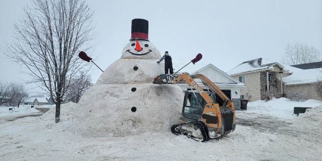 Eric Fobbe, a father from Buffalo, Minnesota, stands on an excavator to add finishing touches to 'Frosty Fobbe' snowman he built with his family in Buffalo, Minnesota.